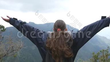 年轻的女徒步旅行者，背包伸向山顶，举起双手。 女游客站在